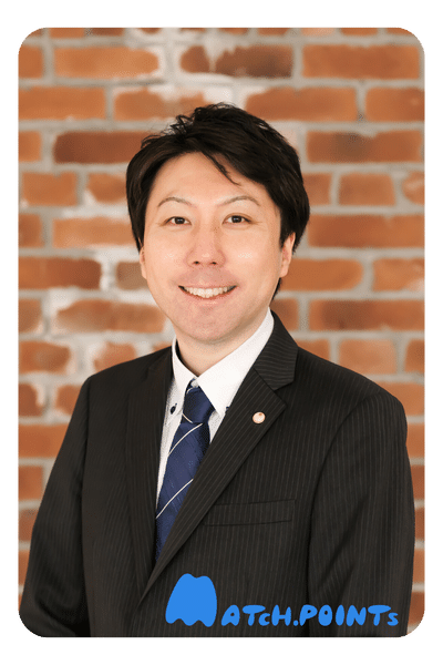 Wakana Shimpei, a Japanese accountant in Sapporo - Japanese man standing in front of a brick wall wearing a thin pinstriped suit with a navy tie and smiling